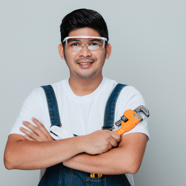 A plumber holding a wrench with his arms crossed over his chest, he is smiling at the camera.